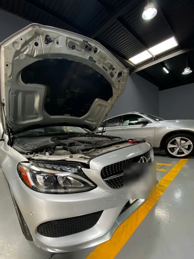 A silver Mercedes C-Class with its bonnet open in a workshop bay, engine bay exposed