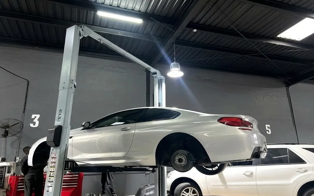 A silver coupe raised on a two-post lift beside a white SUV in the workshop