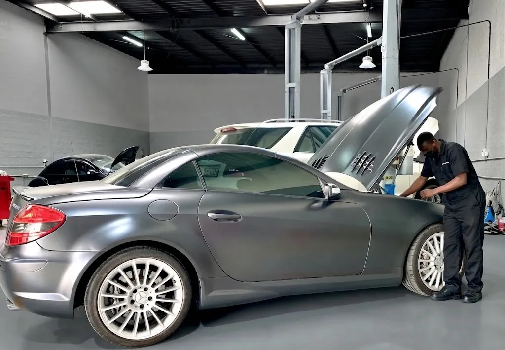 A matte grey Mercedes SLK with its bonnet up while a technician checks the engine bay